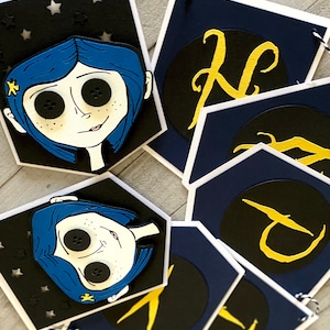 May include: A blue and black banner with a character from the movie "Coraline" and gold letters spelling out the word "Coraline".