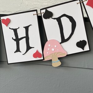 May include: A banner with the letters "H" and "D" in black, with red hearts and black spades. A pink mushroom with white dots and a brown stem is between the letters.
