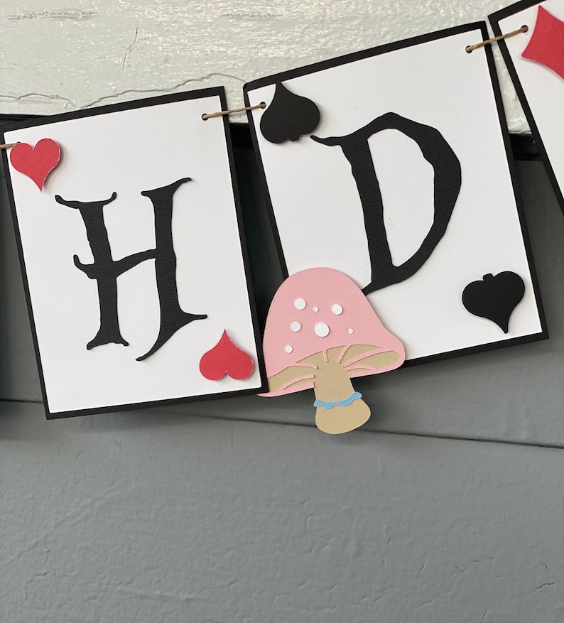 May include: A banner with the letters "H" and "D" in black, with red hearts and black spades. A pink mushroom with white dots and a brown stem is between the letters.