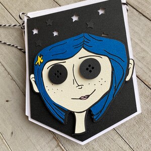 May include: A black and white banner with a cutout of a girl's face. The girl has blue hair, large black eyes, and a small yellow star on her cheek. The banner has a white border and is decorated with white stars.