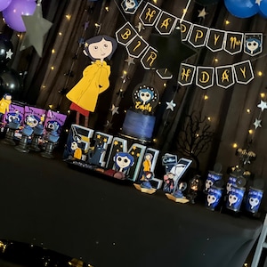 May include: A black table with a black tablecloth decorated for a birthday party. The table is decorated with purple and blue balloons, black stars, and a banner that says "Happy Birthday". There are also cupcakes with a character from the movie "Coraline" on them.