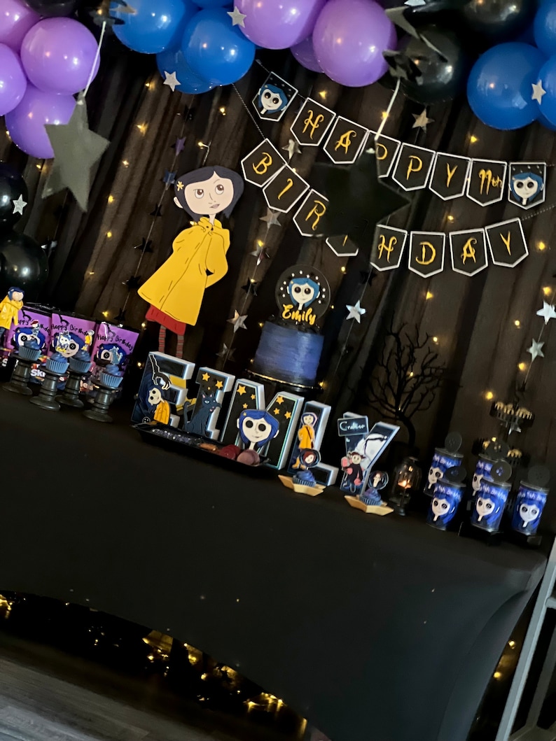 May include: A black table with a black tablecloth decorated for a birthday party. The table is decorated with purple and blue balloons, black stars, and a banner that says "Happy Birthday". There are also cupcakes with a character from the movie "Coraline" on them.