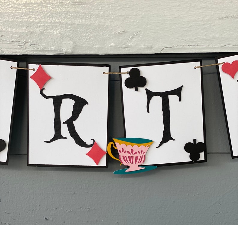 May include: A white banner with black letters spelling out "PARTY" with a teacup and saucer, red and black playing card symbols, and a string running through the top.