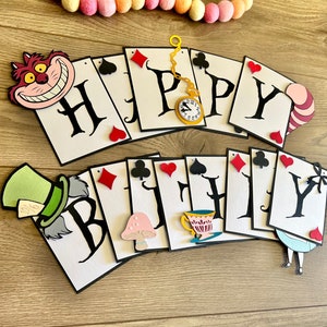 May include: A white and black card banner with the words "Happy Birthday" in black. The banner is decorated with characters from Alice in Wonderland, including the Cheshire Cat, the Mad Hatter, and the Queen of Hearts.