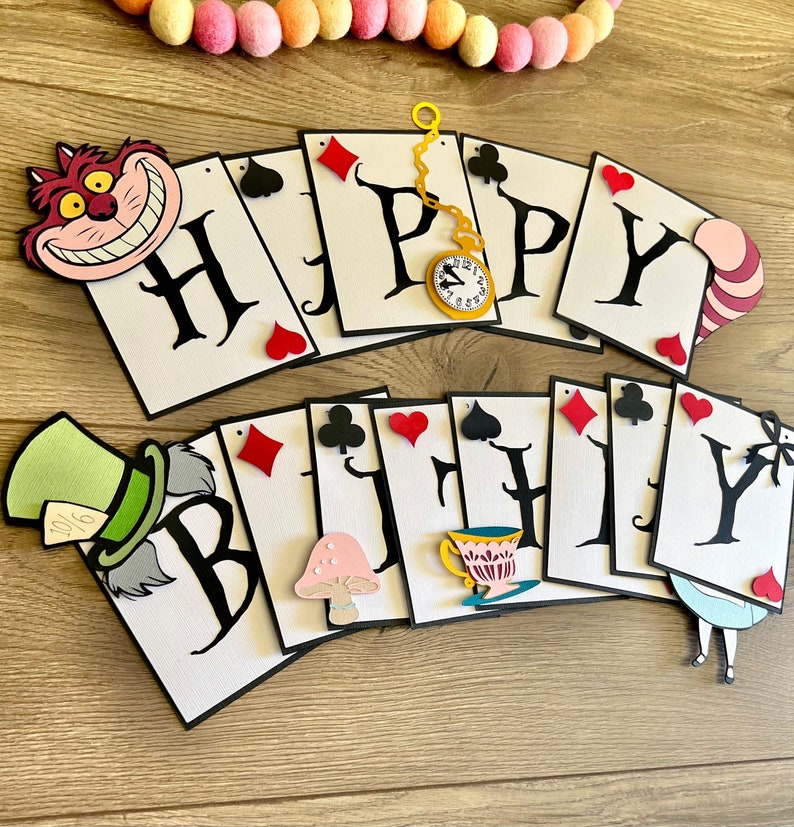 May include: A white and black card banner with the words "Happy Birthday" in black. The banner is decorated with characters from Alice in Wonderland, including the Cheshire Cat, the Mad Hatter, and the Queen of Hearts.