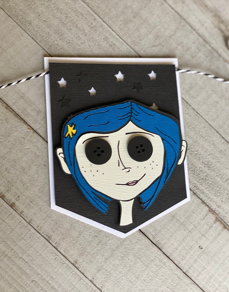 May include: A black and white banner with a cutout of a girl with blue hair and large black button eyes. The banner has a black background with white stars cut out.