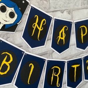 May include: A blue and white banner with the words "Happy Birthday" in gold letters on black circles. The banner is decorated with a character from the movie "Coraline".