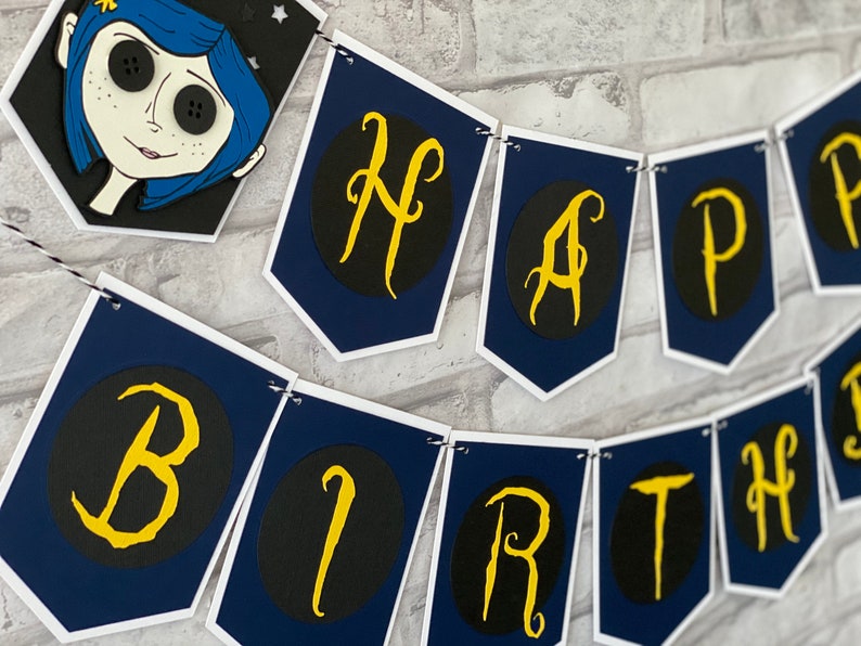 May include: A blue and white banner with the words "Happy Birthday" in gold letters on black circles. The banner is decorated with a character from the movie "Coraline".