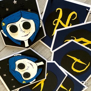 May include: A blue and black banner with a character from the movie "Coraline" and gold letters spelling out the word "N-I-G-H-T".