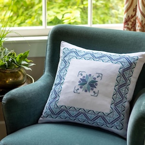 May include: A teal blue armchair with a white cushion featuring a blue and white embroidered geometric design.