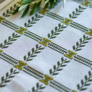 May include: White table runner with a green and yellow embroidered leaf pattern.