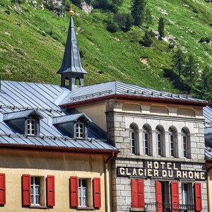May include: A grey stone building with a slate roof and red shutters. The building has a sign that reads "Hotel Glacier du Rhone".