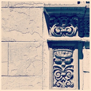 May include: A close-up of a white wall with a decorative, blue-grey, carved stone element. The stone element has a floral design with a central motif that resembles a stylized flower.