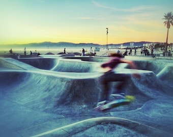 Peut inclure: Une personne fait du skateboard dans un skatepark avec une rampe en béton et une vue sur l'océan en arrière-plan. Le ciel est d'un orange et d'un jaune vifs.