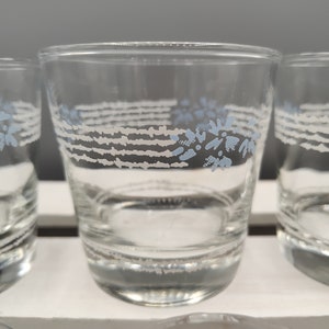 Puede incluir: Vasos de vidrio transparente con un diseño floral y lineal en azul claro y blanco. Los vasos están dispuestos sobre una superficie blanca, mostrando su diseño simple pero elegante. Perfectos para servir bebidas.