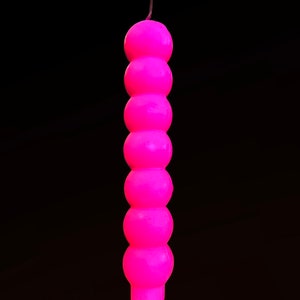 May include: A pink candle with a round, segmented design. The candle is tall and slender, with a pointed top.