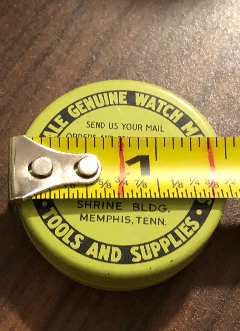 May include: A yellow metal container with black text that reads "ALE GENUINE WATCH M" and "TOOLS AND SUPPLIES". The container also has the text "SEND US YOUR MAIL" and "SHRINE BLDG. MEMPHIS, TENN."