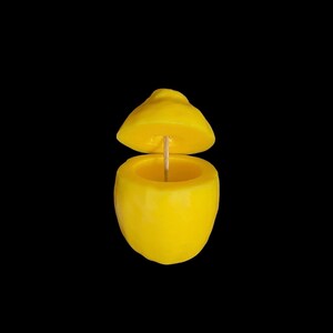 May include: A yellow lemon-shaped candle with a wick sticking out of the top. The candle is split in half, revealing the inside.