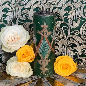 May include: A green candle with gold glitter and a decorative design, surrounded by yellow and white roses and US dollar bills.