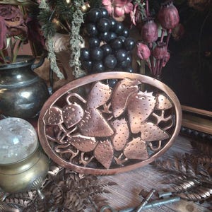 May include: An oval copper-colored tray with a strawberry design. The tray features detailed cutouts of strawberries and leaves. The image also includes decorative elements like a crystal ball, keys, and dried flowers, creating a vintage aesthetic.