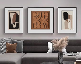 May include: Three framed abstract art prints with geometric shapes in brown, black, and white. The prints are hung on a white wall above a gray sectional sofa with pillows.