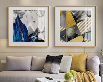 May include: Two abstract art prints in gold frames. The print on the left features a blue and gray mountain with gold circles. The print on the right features a geometric design with gold, black, and white accents.