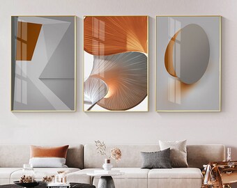 May include: Three abstract art prints with geometric shapes and patterns in shades of gray, white, and orange. The prints are framed in gold.
