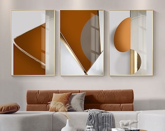Könnte beinhalten: Drei abstrakte geometrische Wandbilder in goldenen Rahmen. Die Drucke zeigen einen weißen Hintergrund mit überlappenden Formen in Braun- und Goldtönen.
