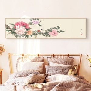 May include: A long, horizontal painting of pink, white, and purple peonies with green leaves and a small butterfly. The painting is framed in a thin, gold frame and is hanging on a white wall above a bed with a wooden headboard.