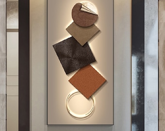 May include: Abstract wall art featuring a geometric design with brown, beige, and black shapes. The shapes are layered and overlap, creating a dynamic and modern look. A gold ring is incorporated into the design, adding a touch of elegance.