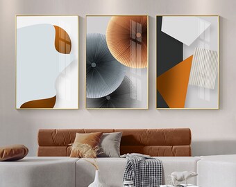 Könnte beinhalten: Drei abstrakte Kunstdrucke in goldenen Rahmen mit geometrischen Formen und Mustern in Weiß-, Grau-, Schwarz-, Orange- und Brauntönen.