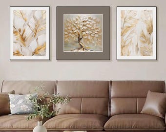 May include: Three framed wall art pieces. The artwork features abstract designs with gold and white leaf and tree motifs. The frames are black, and the art is displayed above a brown leather sofa and glass coffee table.