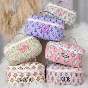 May include: A collection of quilted cosmetic bags in various colors, including pink, green, and blue. Each bag features a floral pattern and a personalized monogram or name in embroidered lettering. The bags have a zippered closure and a small handle.