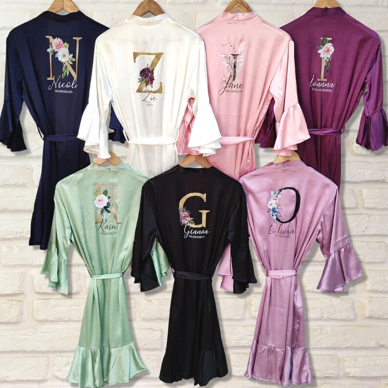 May include: Six satin robes in different colors with floral designs and a gold letter on the back. The robes have ruffled sleeves and a ruffled hem. The letters on the robes are N, Z, J, I, R, and G.