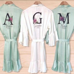 May include: Three satin robes with ruffled hems and bell sleeves. The robes are personalized with a large initial and the name of the wearer. The robes are in mint green and white.