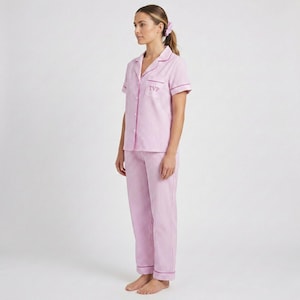 May include: A pink and white striped pajama set. The short-sleeved top has a collared neckline and the initials "TVP" embroidered on the chest. The pajama pants are long and have a matching stripe pattern. The set is trimmed with a darker pink piping.