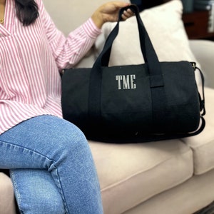 May include: A black canvas duffel bag with a white embroidered monogram "TME".