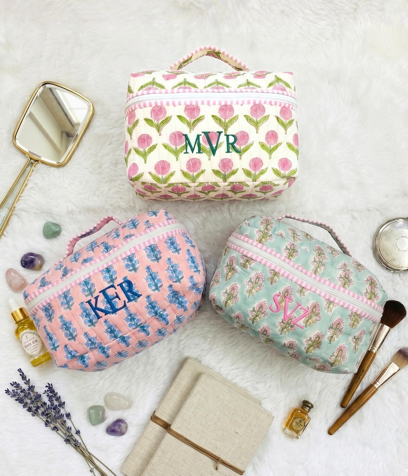 May include: Three quilted cosmetic bags with floral patterns and personalized initials. The bags feature a handle, zipper closure, and a pink and white color scheme. The bags are on a white surface with beauty accessories.