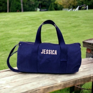May include: A navy blue canvas duffel bag with a pink embroidered name "JESSICA" on the front.