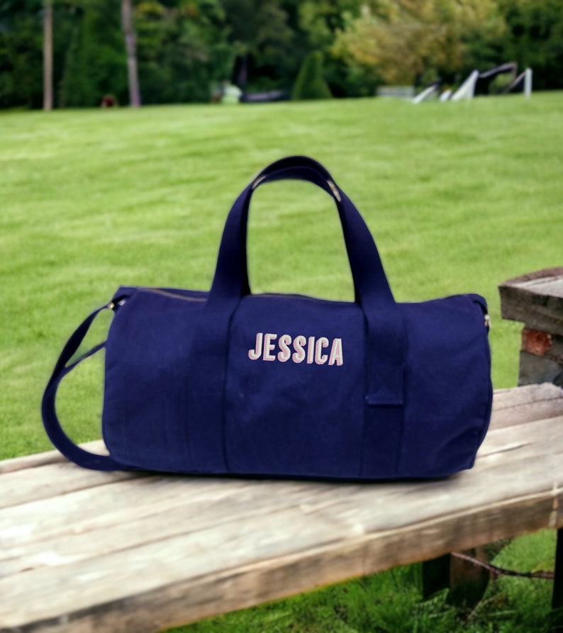 May include: A navy blue canvas duffel bag with a pink embroidered name "JESSICA" on the front.