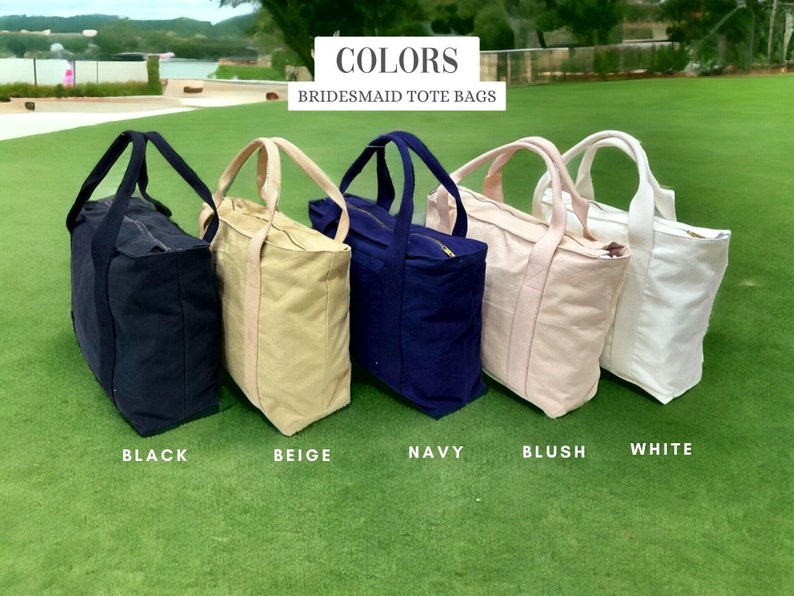 May include: Five canvas tote bags in black, beige, navy, blush, and white are displayed on green grass. Each bag has a matching handle and a zipper closure. The text "COLORS BRIDESMAID TOTE BAGS" is at the top of the image.
