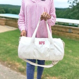 May include: White canvas duffel bag with a pink embroidered monogram "MPS".