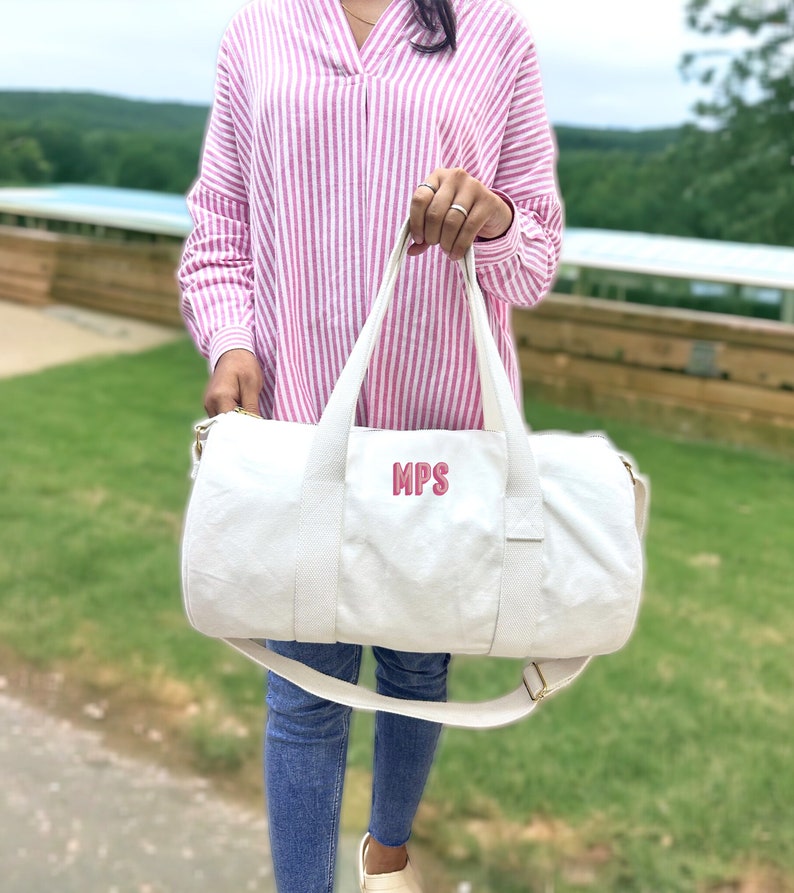 May include: White canvas duffel bag with a pink embroidered monogram "MPS".