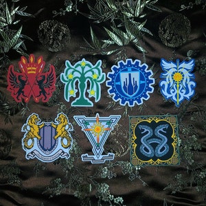 May include: Eight colorful stickers with different designs, including a tree, a snake, a crown, and a gear. The stickers are on a brown fabric background.