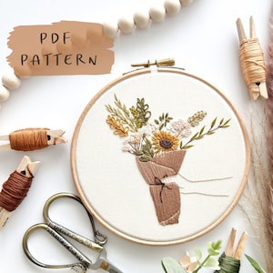 May include: A PDF pattern for an embroidery hoop art project featuring a bouquet of flowers in shades of brown, yellow, and white, wrapped in brown paper. The text "PDF PATTERN" and "INSTANT DOWNLOAD" are visible in the image.