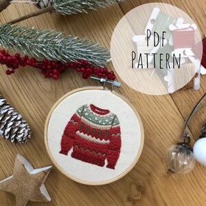 Puede incluir: Patr&oacute;n de su&eacute;ter de Navidad bordado en un aro. El su&eacute;ter es rojo con detalles en verde, blanco y marr&oacute;n. El patr&oacute;n est&aacute; disponible para descargar en PDF.
