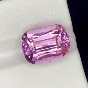 May include: A large, rectangular, faceted gemstone with a pink hue. The gemstone is set on a white background.