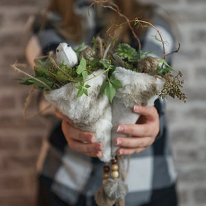 Könnte beinhalten: Ein weißer Kunstfellkegel mit einer kleinen weißen Vogelfigur und Grünzeug im Inneren. Der Kegel ist mit braunen Perlen und einem braunen Quasten verziert.