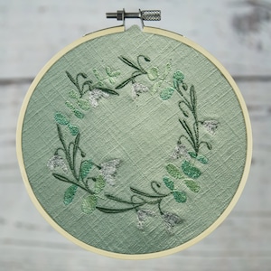 May include: A green embroidery hoop with a white floral design. The flowers are embroidered in white and green thread.