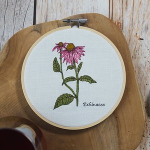 May include: Embroidered hoop art featuring a pink and green echinacea flower with the text "Echinacea" below it.